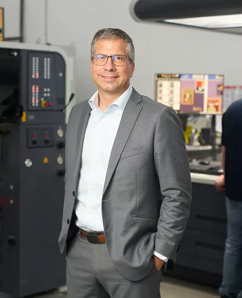 Chad Friesen standing in front of a modern printing press.